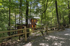 Une cabane en bois, entourée d’une forêt, avec un chemin de gravier menant à l’entrée.