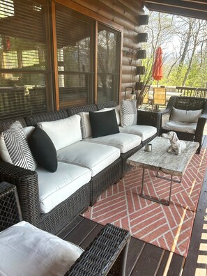 A log cabin with a sofa set, wicker chairs, and a table with a metal frame. - Secluded Cherry Log Cabin - Sauna - Hot Tub - Putting Green (Blue Ridge)