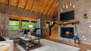 A cozy living room with a fireplace, wooden beams, a sofa, a coffee table, and a television.