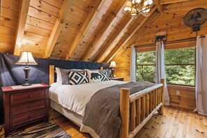 Quarto de cabana de madeira com cama, abajures, cômoda e janela com cortinas.