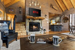 A cozy living room with a fireplace, a television mounted above it, and a coffee table with two mugs.