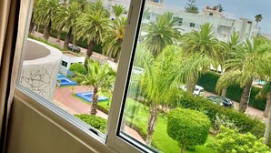 A view from a window overlooking a well-maintained outdoor area with palm trees, a paved walkway, and a building with satellite dishes. - Résidence Beach palace 1, apartment at the beach  (Mohammédia)