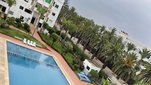 A swimming pool surrounded by palm trees and a building with multiple balconies. - Résidence Beach palace 1, apartment at the beach  (Mohammédia)