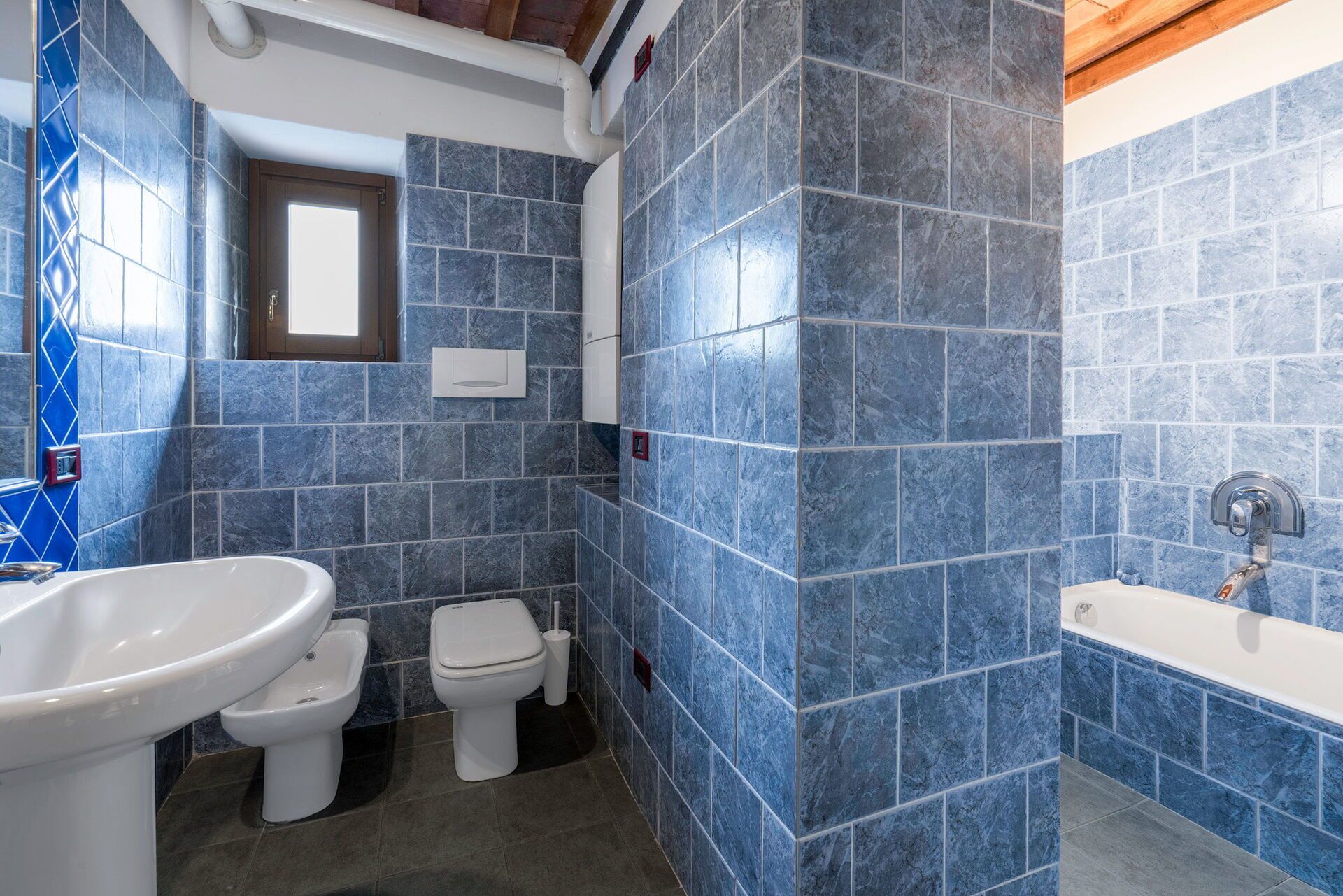A bathroom with blue tiles, a white sink, a toilet, and a bathtub.