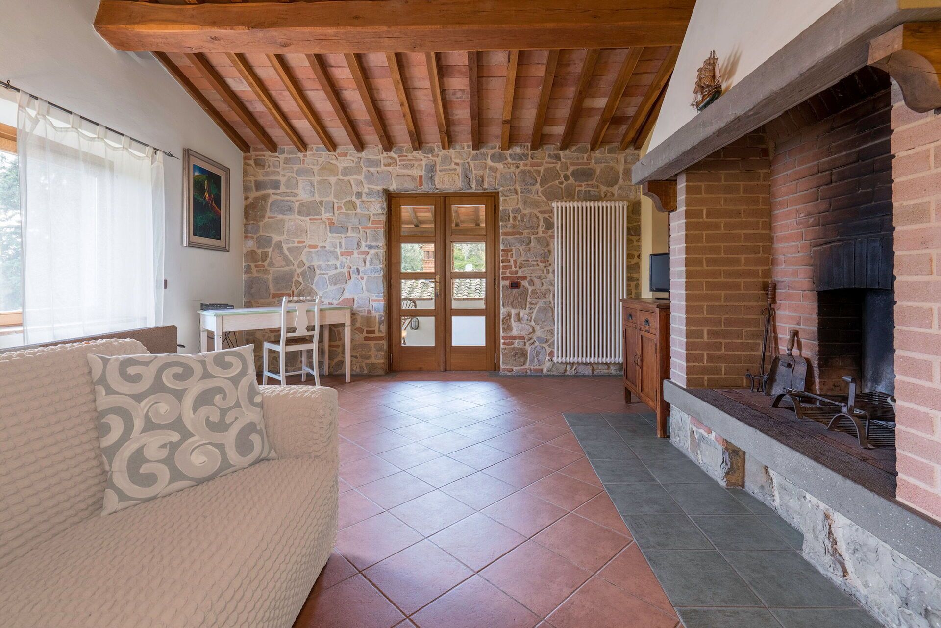 A cozy room with a stone wall, a fireplace, a wooden ceiling, and a tiled floor.