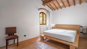 Un dormitorio con cama de madera, una silla, un ventanal con vistas y un radiador.