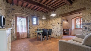 Una habitación rústica con paredes de piedra, un comedor, un sofá y un televisor.