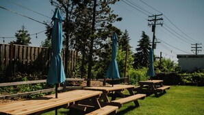 Un área de picnic con mesas de madera y sombrillas azules, rodeada por una valla de madera y árboles.