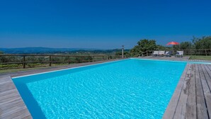 A rectangular swimming pool with a wooden deck, surrounded by a wooden fence, and a red umbrella.