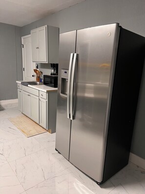 A kitchen with a stainless steel refrigerator, white cabinets, a microwave, and a coffee maker. - Mini Apartamento Encantador (Spring Hill)