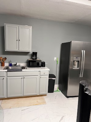 A modern kitchen with a stainless steel refrigerator, a coffee maker, and a trash bin.