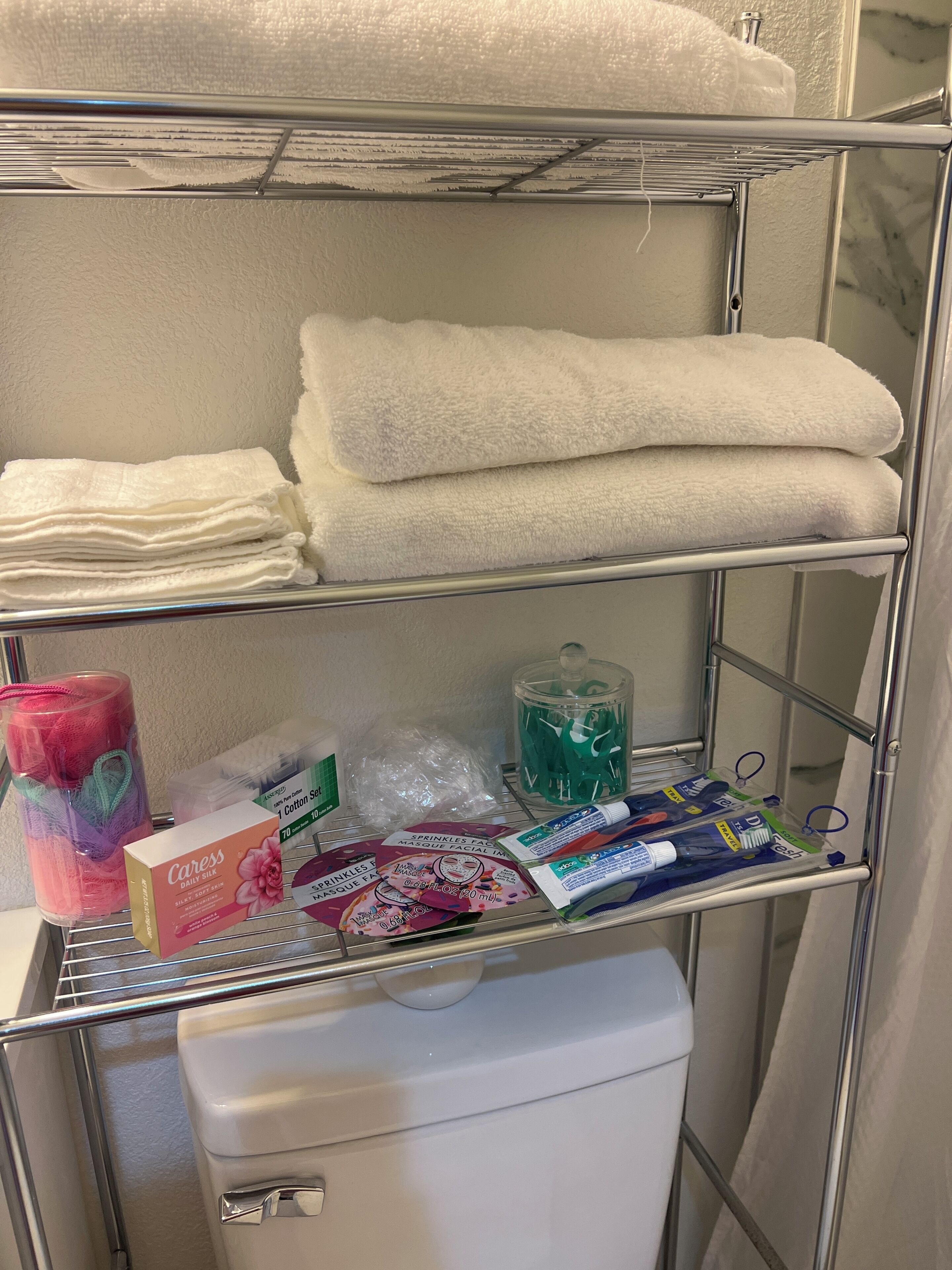 A bathroom with a shelf holding towels, a toilet, and toiletries.