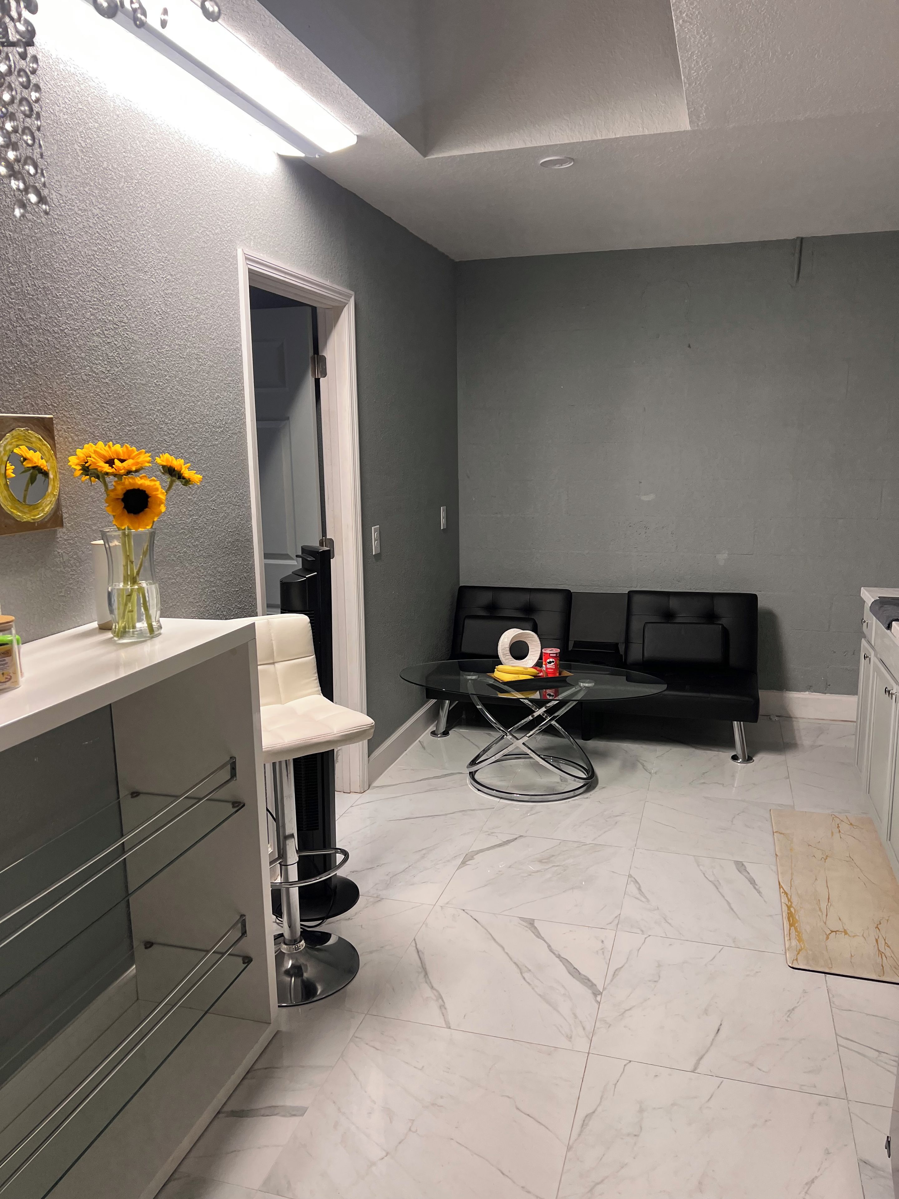 Un baño moderno con un tocador blanco, una mesita de vidrio con un anillo decorativo y un espejo con adorno de girasol.
