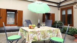 Eine Terrasse im Freien mit einem Tisch für zwei Personen, einer Champagnerflasche und einem Obstkorb.