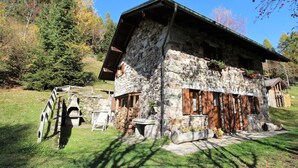 Ein Steinhaus mit geneigtem Dach, hölzernen Fensterläden und einer kleinen Veranda.