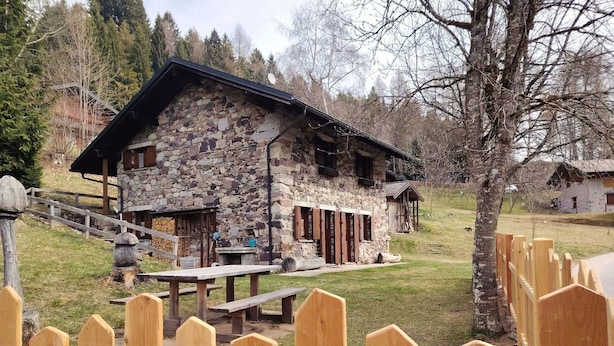 Ein Steinhaus mit einer Holzveranda, einem Picknicktisch und einem Holzzaun.