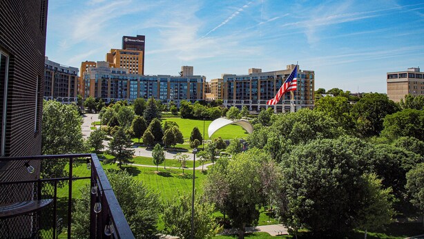 Un paisaje urbano con edificios modernos, una gran bandera estadounidense y una zona verde de parque.