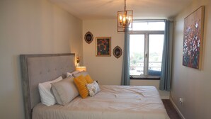 Un dormitorio con una cama grande, un candelabro, una ventana con cortinas y obras de arte en las paredes.