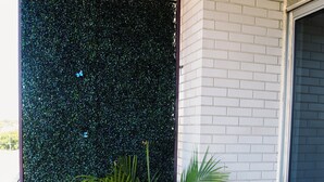 Una planta en maceta en un balcón con un muro verde y una pared de ladrillo blanco.