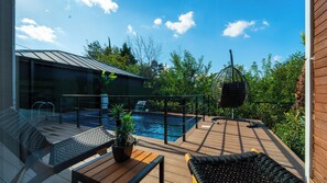A poolside area with a glass balustrade, a hanging chair, and a wooden deck.