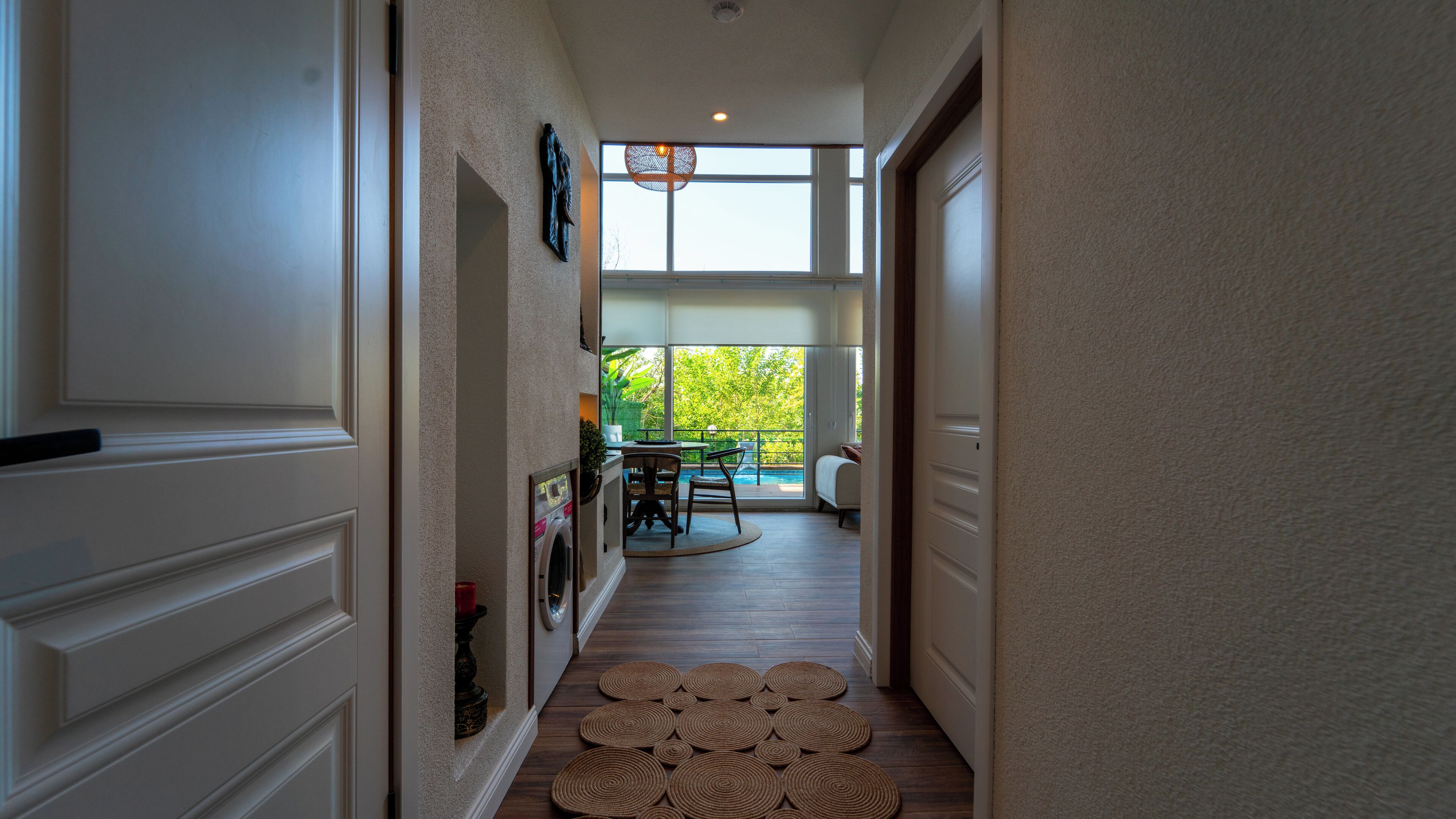 A hallway leading to a dining area with a view of a swimming pool and greenery.