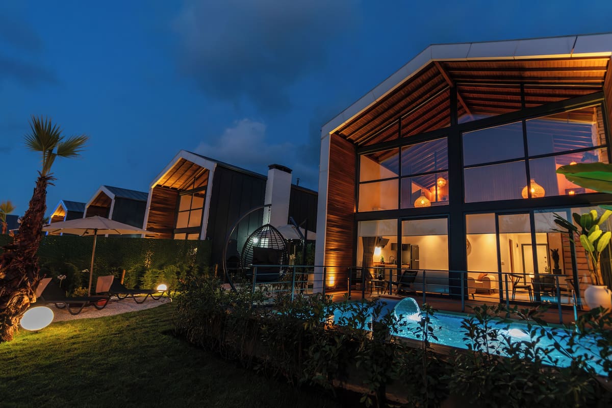 A modern house with a large glass facade, a swimming pool, and a well-lit interior.