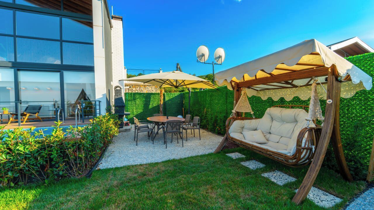 A modern outdoor seating area with a swing chair, a round table, and umbrellas.