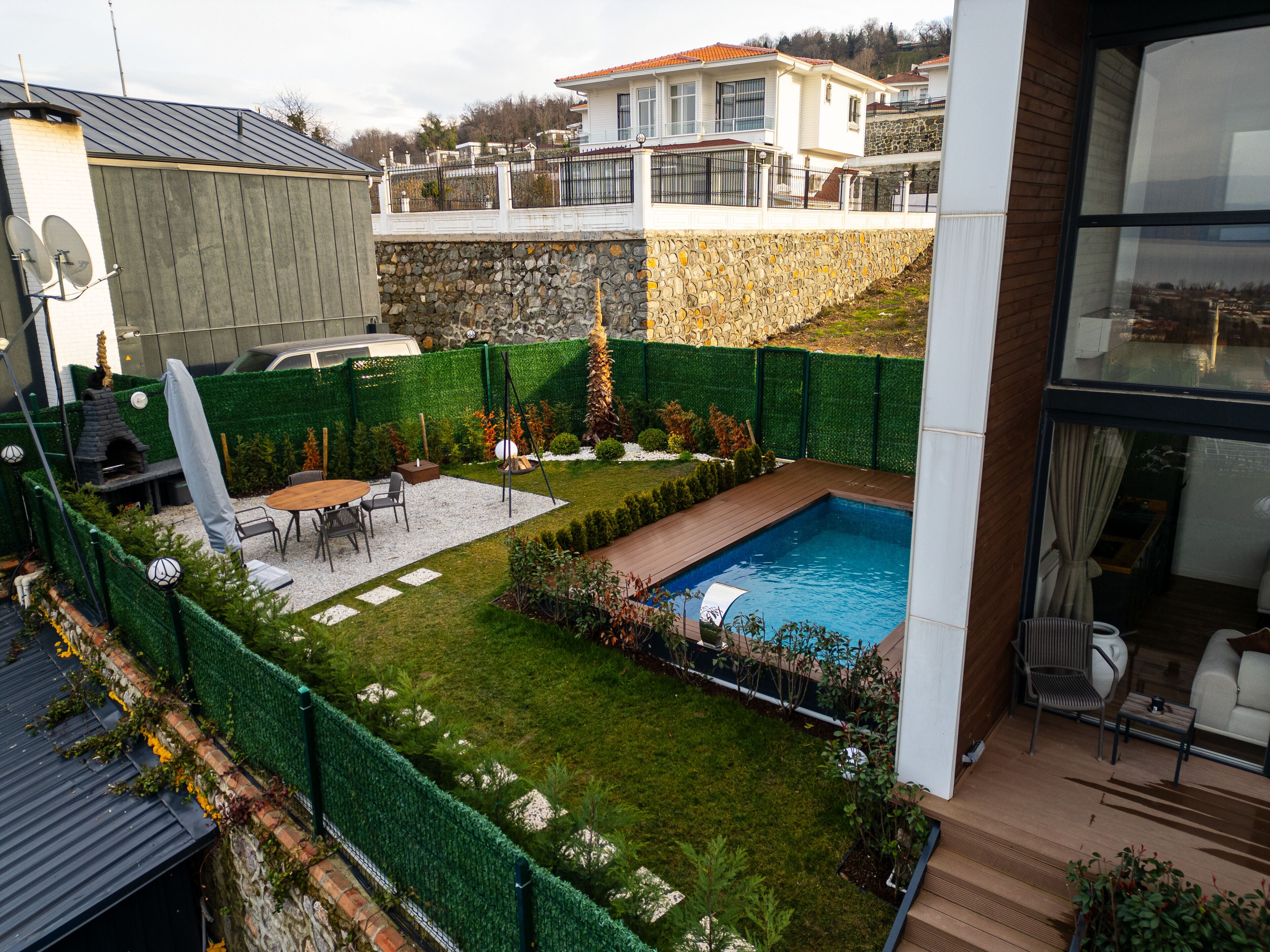 Ein Garten mit Swimmingpool, Grillplatz und einer Steinmauer.
