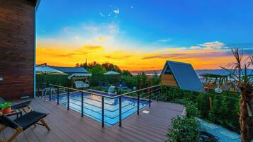 Relax on the deck overlooking the pool, surrounded by lush greenery and a modern building.