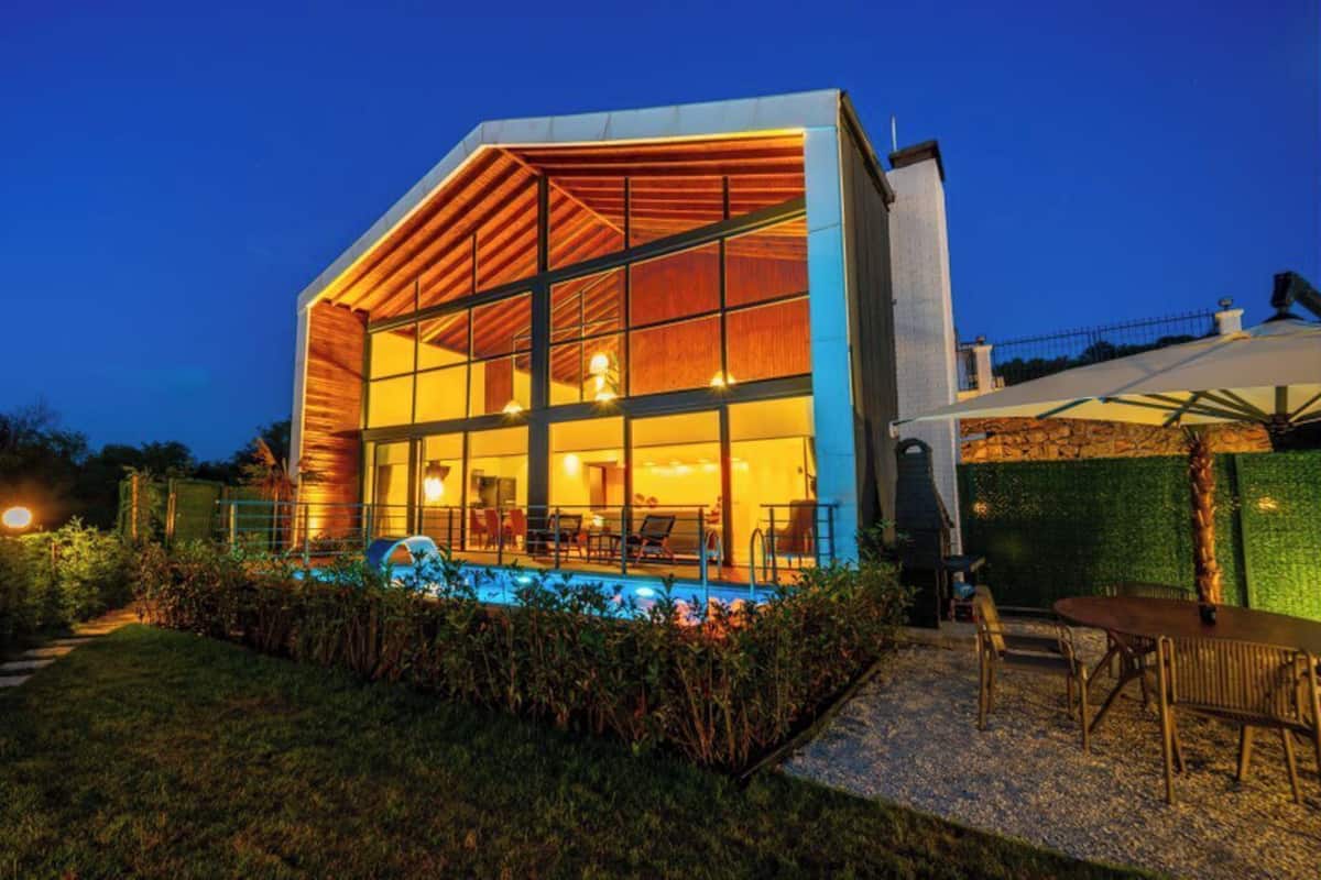 A modern house with a large glass facade, a swimming pool, and outdoor seating.