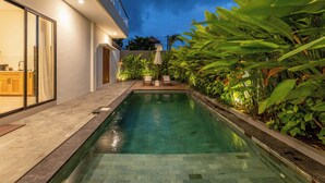 Una casa moderna con piscina, un patio con sillas y abundante vegetación.