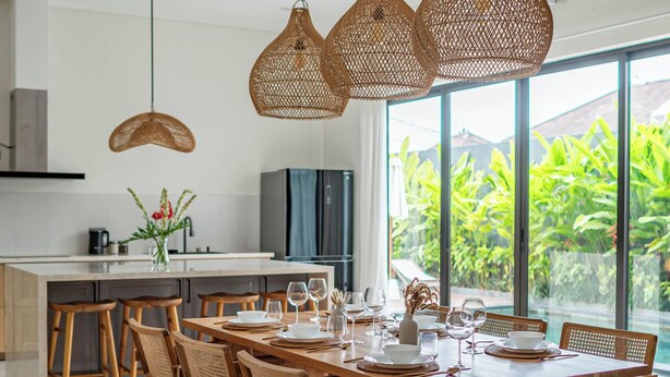 Una cocina moderna con una isla grande, sillas de madera y lámparas de ratán colgantes.