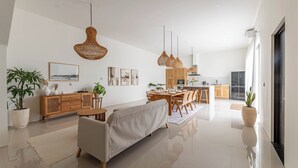 Un espacio moderno y abierto para sala y comedor, con sofá, mesa de comedor y lámparas de mimbre colgantes.