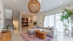 Una sala de estar moderna con sofá, una mesita de centro, un tapete estampado, una escalera y una planta grande en maceta.