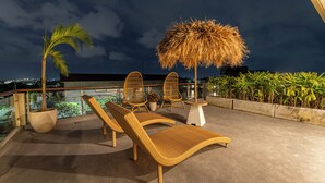 Terraza en la azotea con sillones de descanso, una sombrilla de paja y plantas en macetas.