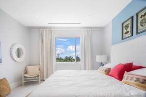 Ein Schlafzimmer mit einem großen Bett, einem Sessel, einem Fenster mit Vorhängen und gerahmten Bildern an der Wand.