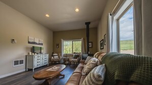 Un salon spacieux avec un canapé en cuir, une table basse en bois et un téléviseur posé sur un meuble blanc.