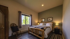 Une chambre avec un lit en bois, une chaise, une table de chevet et une fenêtre avec des rideaux.