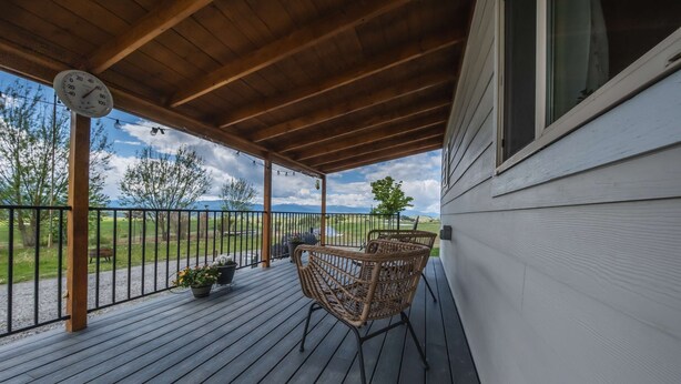 Une terrasse en bois avec une chaise en osier et une horloge, donnant sur une zone herbeuse.