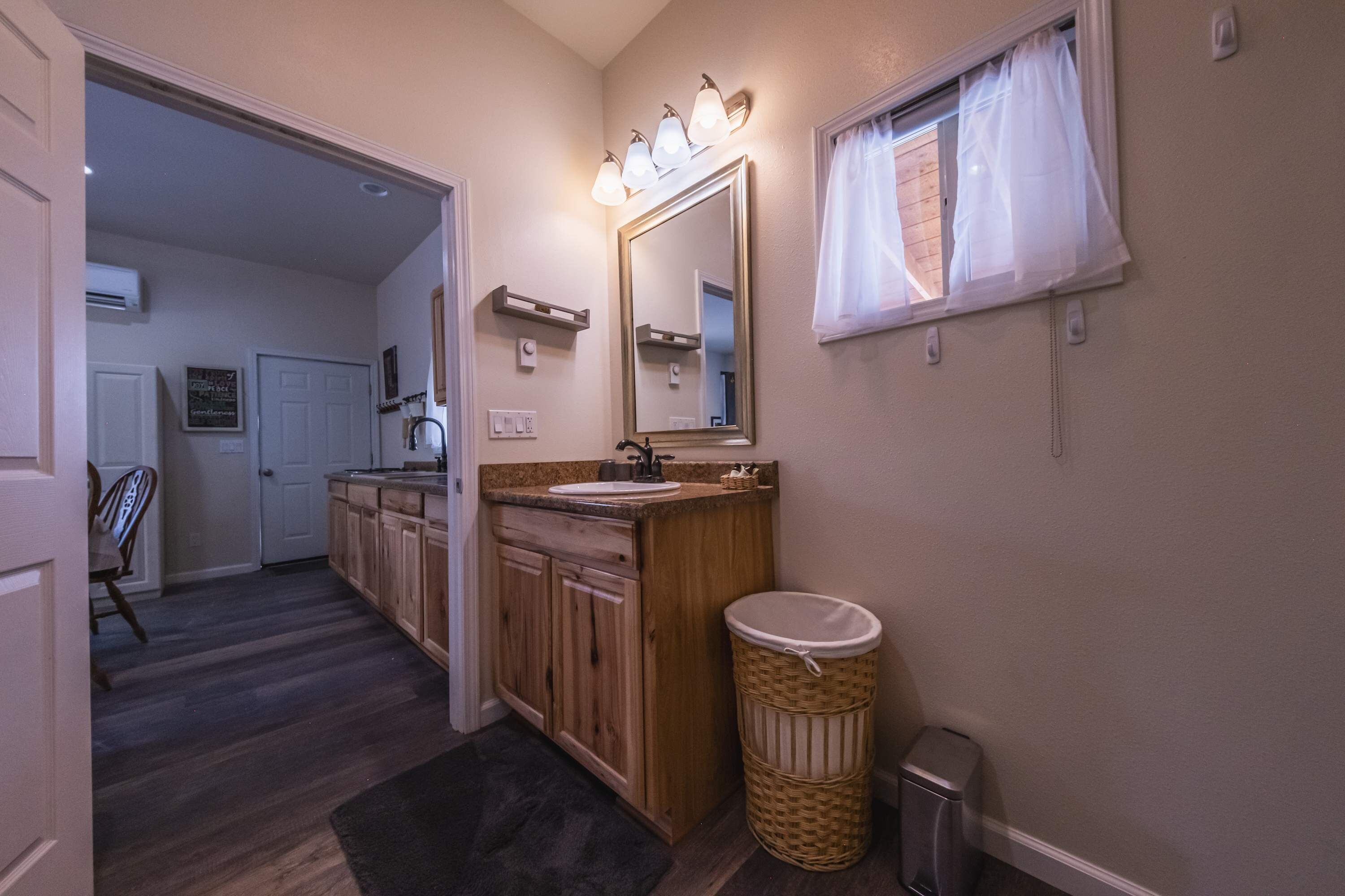A bathroom with a wooden vanity, a sink, a mirror, and a trash can.