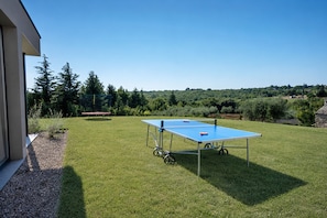Ett bordtennisbord står på en gräsyta utomhus, med en byggnad på ena sidan.