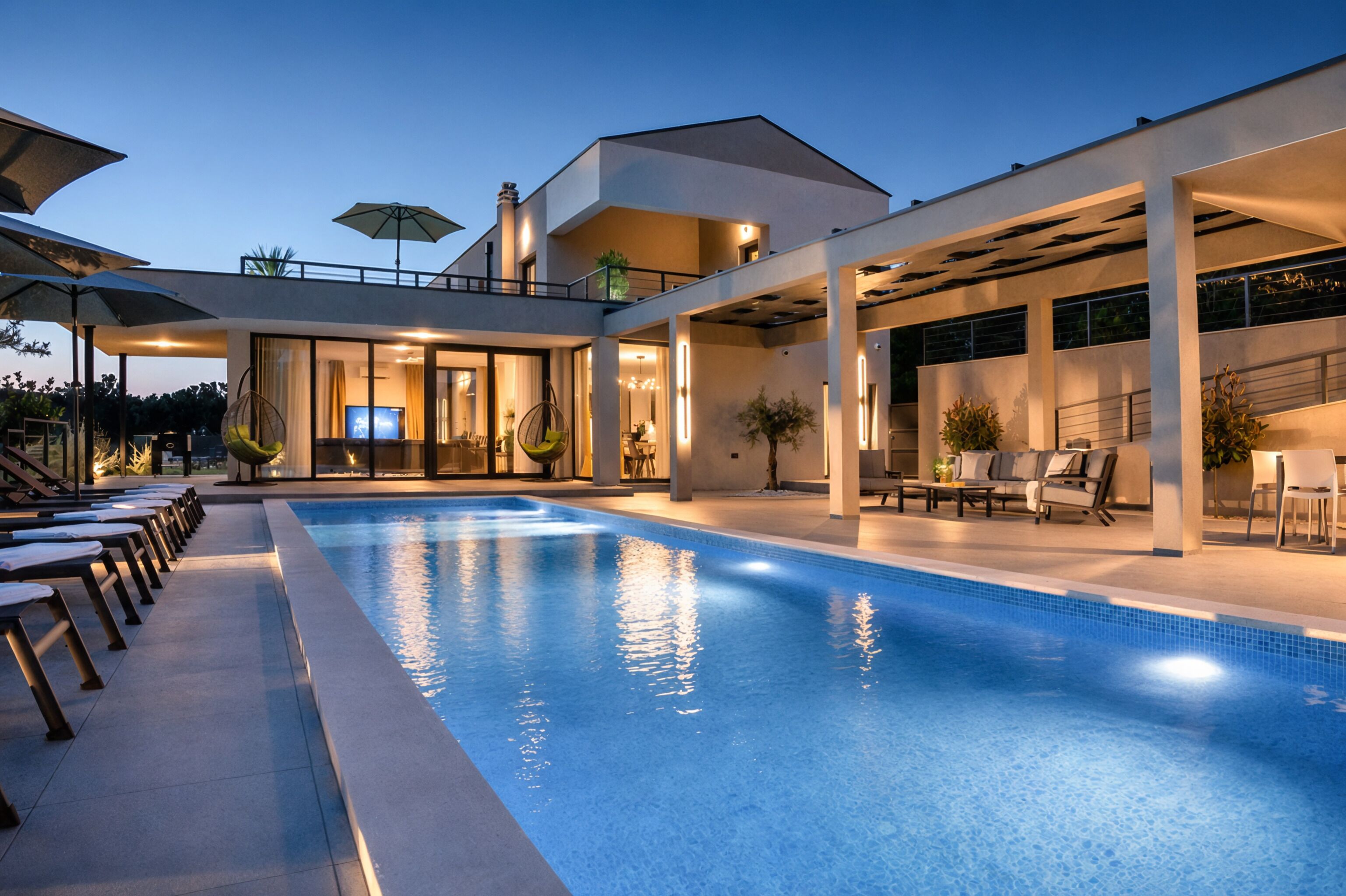 A modern poolside area with a clear blue pool, lounge chairs, and a covered seating area.