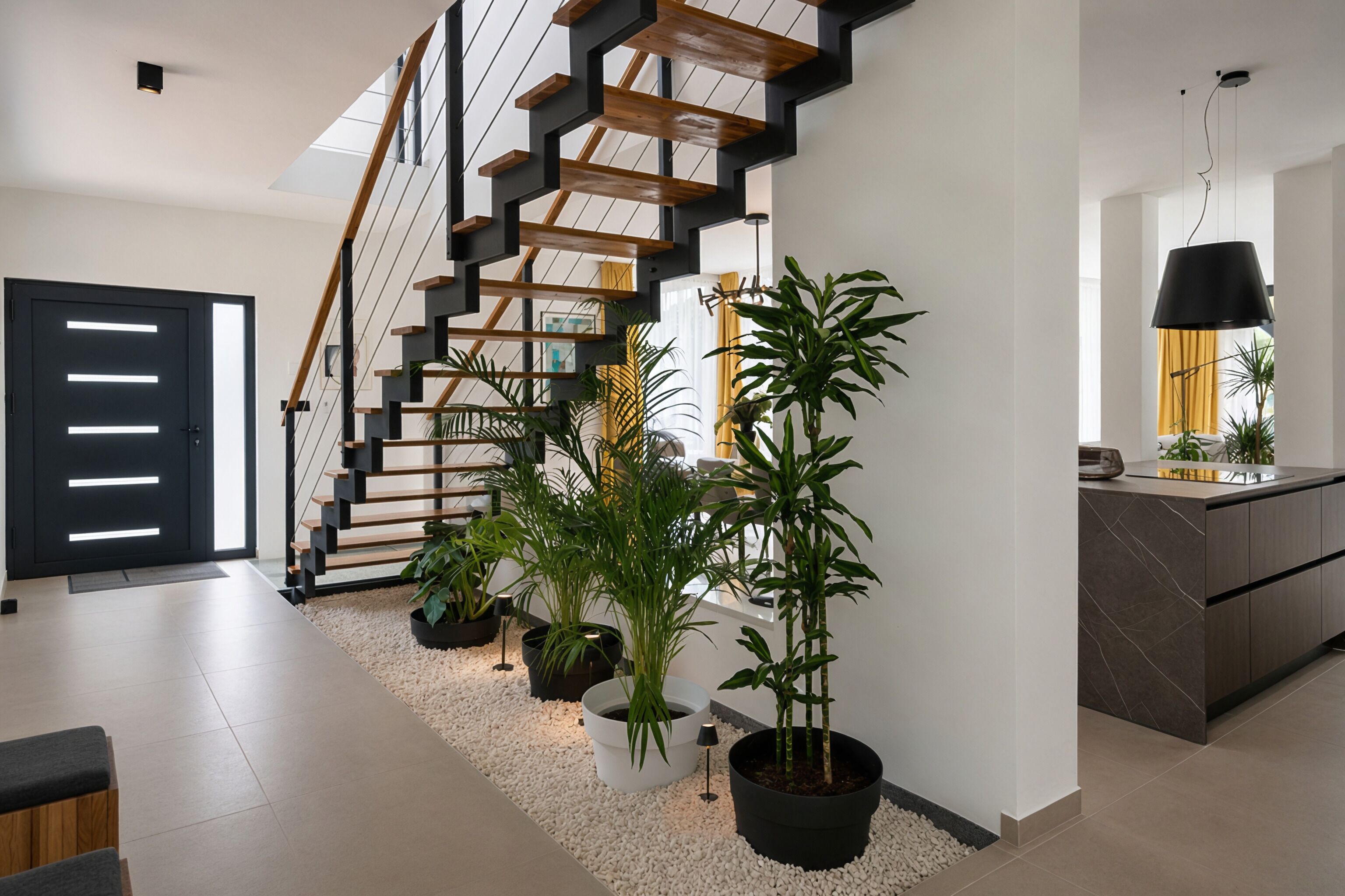 Un intérieur moderne avec un escalier, des plantes en pot et un coin cuisine.