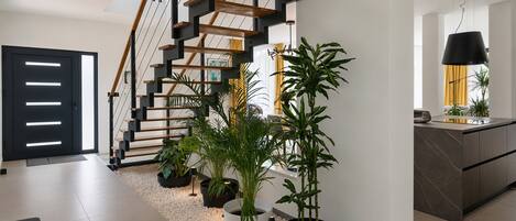 A modern interior with a staircase, potted plants, and a kitchen area.