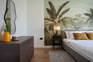 Ein Schlafzimmer mit Bett, Nachttisch, Lampe und einer Wandmalerei von Blättern.