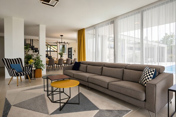 A modern living room with a sofa, a coffee table, and a dining area with chairs and a table.
