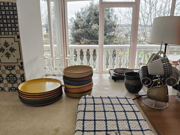 Comedor con vistas al exterior, que incluye una mesa con platos apilados, vasos y un tapete decorativo.