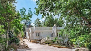 Un bâtiment à deux étages, doté d’une cheminée en pierre, entouré d’une végétation luxuriante et d’arbres.