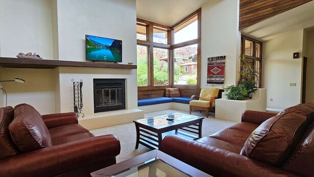 A living room with leather sofas, a fireplace, a television, and large windows offering a view of the outdoors. - Sedona Sunrise (Sedona)