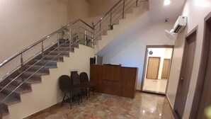 A lobby with a marble floor, a staircase, a reception desk, and a door leading to another room. - Hotel Shiv Inn By T And M Hotels (Haridwar)
